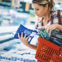 Gepanscht, geregelt und gegessen Frau steht im Supermarkt mit Einkaufskorb vor der Gefriertruhe und studiert die kleingedruckten Angaben eines Lebensmittels.