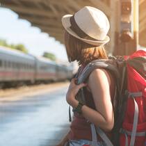 Besser als fliegen Reisende mit dem Rucksack, die auf einen Zug am Bahnhof wartet. Zug im Hintergrund zu sehen.