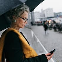 6 Meteo-Apps und ihre Vorteile im Vergleich Frau steht im Regen und prüft ihr Smartphone