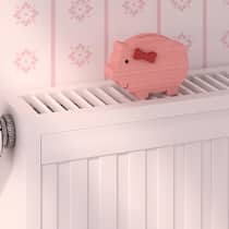 Frieren zum Sparen? Das muss nicht sein Ein pinkfarbiges Holzsparschwein steht auf einem Heizkörper.