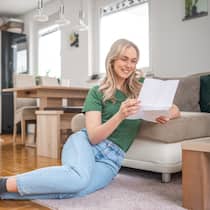 Erhalte ich die Säule 3a meines Vaters? Eine junge Frau sitzt auf dem Fussboden ihrer Wohnung und freut sich über einen Brief, den sie gerade am Lesen ist. Kann die Tochter das Guthaben aus der Säule 3a des Vaters erben, wenn dieser nichts im Testament vermerkt hat?