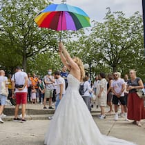 Darum geht es bei der «Ehe für alle» Frau in Hochzeitskleid hält in Lausanne bunten Regenschirm in die Luft