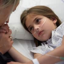 Wie lange darf ich mit meinem kranken Kind zuhause bleiben? Ein Mädchen mit Atemmaske hält die Hand ihrer Mutter. Wie die Betreuung kranker Kinder geregelt ist.