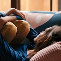 Gefangen in der Selbstreflexion Einsame Frau umklammert auf dem Sofa liegend ihre Knie.