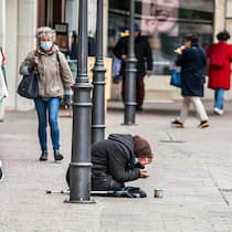 Soll ich Geld geben? Eine Bettlerin hat sich auf eine belebte Fussgängerstrasse hingekniet, ihr Blick ist nach unten gerichtet und die Menschen gehen an ihr vorbei.