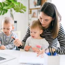 Wer kommt für Mutter und Kinder auf? Eine alleinerziehende Mutter arbeitet am Laptop und betreut nebenbei ihre beiden Kleinkinder.