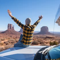 5 Tipps, damit die Sommerferien 2022 nicht zu teuer werden Mann sitzt auf Kühlerhaube seines Campers in den USA