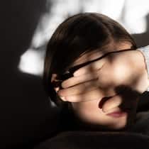 Emilia hat Angst Mädchen in halbdunklem Raum hält sich den Arm vor die Augen. Panikattacken, Depressionen, Selbstverletzungen – psychische Störungen bei Kindern und Jugendlichen nehmen zu. Ebenso verlängern sich die Wartezeiten bei Psychologinnen und psychiatrischen Einrichtungen. Warum?