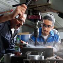 Neue Ansätze sollen jungen IV-Bezügern helfen 2T97J4G Instructor with trainee spraying lubricant on drill bit at workshop