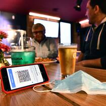 Das bedeutet die Ausweitung der Zertifikatspflicht Auf einem Restauranttisch liegt eine Schutzmaske sowie ein Smartphone, auf welchem ein QR-Code eines Covid-Zertifikats zu erkennen ist.