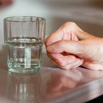 Sterbehilfe auch im Pflegeheim? Was man dazu wissen muss Hand der Bewohnerin einer Seniorenresidenz liegt neben einem Wasserglas