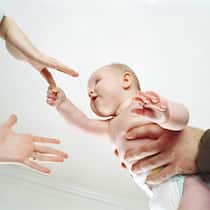 «Elternsein ist nicht schwieriger als früher. Nur anders» Zwei Paar Hände greifen nach Baby. Maternal Gatekeeping, Mental Load und Erschöpfung - Ein Gespräch mit Psychologin Valentina Rauch-Anderegg über die Tücken des modernen, gleichberechtigten Elternlebens.