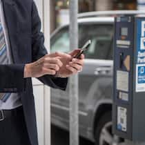 85 statt 5 Franken bezahlt – Polizei bleibt streng Zu sehen ist ein Mann im Anzug, der gerade etwas auf seinem Handy eintippt. Er befindet sich direkt neben einer Säule für das Bezahlen von Parkgebühren.