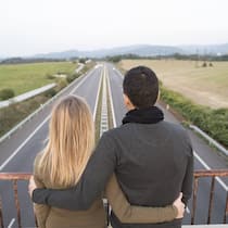 «Wie können wir unsere Situation verbessern?» Ein Paar steht auf einer Autobahnüberführung, der Blick auf die weite Strasse gerichtet und hält sich dabei in den Armen.