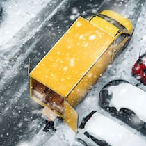 Das lange Warten aufs Geschenk Ein gelber Lieferwagen steht auf einem verschneiten Parkplatz zwischen anderen Autos.