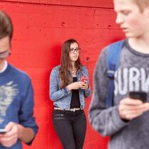 Rachepornografie – was man als Betroffene tun kann Jugendliche schaut betroffen, während zwei Jungs über verbreitete Inhalte auf dem Handy sprechen.