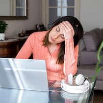 Was tun, wenn alles einfach nur noch besorgniserregend ist? Eine junge Frau sitzt an einem Glastisch mit sorgenvoller Miene, vor ihr ist ein Laptop aufgeklappt.