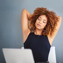 So kommt Bewegung ins Büro Eine Frau sitzt vor dem Laptop und streckt sich.