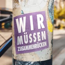 Wir werden immer mehr – was heisst das? Sticker mit Aufschrift: Wir müssen zusammenrücken