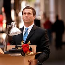 Das sind die Regeln bei Entlassung Geschäftsmann im Anzug hält eine Kartonschachtel mit persönlichen Gegenständen seines Arbeitsplatzes in der Hand und verlässt die Geschäftsräume.