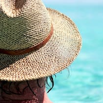 Vor diesen Reisekrankheiten sollten Sie sich schützen Mann mit Sonnenhut blickt aufs offene Meer