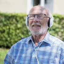 Heilsame Töne Ein älterer Mann sitzt im Garten und hört Musik.