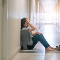 Wie können Angehörige damit umgehen? Eine Frau sitzt in einer Klinik auf dem Boden und schlägt die Hände vors Gesicht.