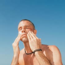 Günstigste Sonnencreme schlägt im Test teure Marken Man applying sunscreen to face against blue sky copy space, outdoor skincare and sun protection Florida Gulf Coast.