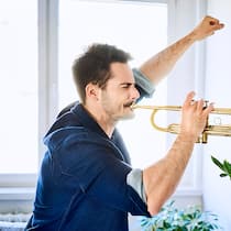 Wer will Krach? Ein junger Mann spielt mit erhobener Faust Trompete in der Wohnung