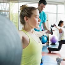 Muskeln ohne Katerstimmung Eine Frau trainiert mit einer Hantel und der Trainer gibt Anweisungen.