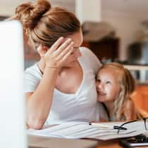 Wie Unverheiratete den Kindesunterhalt berechnen Eine Frau hält ein lächelndes Kind im Arm, während sie am Tisch sitzt und den Kopf aufstützt. Wie man Kindesunterhalt bei Unverheirateten berechnet.