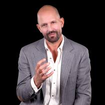 Er deckte Missstände im Spital auf Kandidat André Plass sitzt im weissen Hemd und grauer Anzugsjacke vor schwarzem Hintergrund.