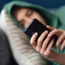 So unterstützen Sie Ihr Kind auf Social Media Ein nicht erkennbarer junger Mann liegt zu Hause seitlich auf dem Sofa und nutzt sein Mobiltelefon zum SMS-Schreiben und Surfen im Internet.
