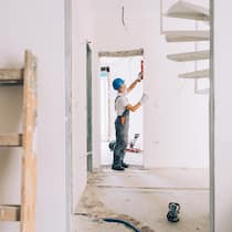 Sanierungsboom – so finden Sie noch Handwerker A construction worker wearing a blue helmet using a leveling tool for walls inside an apartment.
