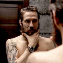 Hau(p)tsache männlich! Hautpflege für Männer: Ein Mann mit Bart betrachtet sich im Spiegel.