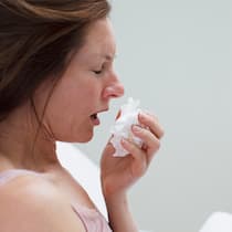 Für vieles ist ein Kraut gewachsen Eine Frau mit Fieberthermometer in der Hand schneuzt sich.