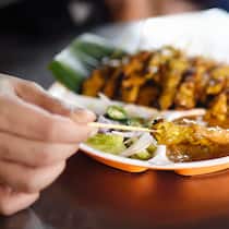 So schlagen die Ferien nicht auf den Magen Ein Mann isst Satay-Spiesse.