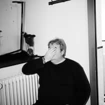 «Ich habe nie alle Ungeimpften als Arschlöcher bezeichnet» Mike Müller sitzt neben einem Radiator und hält sich die Hand vors Gesicht, Schwarz-weiss-Bild