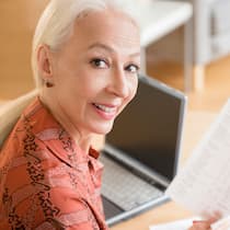So kommen Sie nicht zu kurz Ältere Frau sitzt an einem Tisch. Auf dem Tisch steht ein Laptop und sie hält einen Auszug in der Hand und schaut in die Kamera.