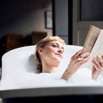 Die Kunst des Müssiggangs Eine Frau liegt in der Badewanne und liest ein Buch