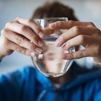Ungemach für Evodrop – die Schlinge zieht sich zu Boy is drinking water from the glass in the kitchen. Focus on glass. Boy is blurred behind.
