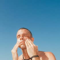 Die günstigste Sonnencreme schlägt im Test teure Marken Man applying sunscreen to face against blue sky copy space, outdoor skincare and sun protection Florida Gulf Coast.