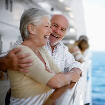 Kreuzfahrer, aufgepasst! Älteres, fröhliches Ehepaar steht an der Reling eines Kreuzfahrtschiffes.
