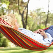 Wie viel und wie lange einzahlen? Rentner liegt in Hängematte auf grüner Wiese.