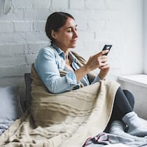 7 Apps für mehr Entspannung Entspannte Frau sitzt mit Handy auf Sofa