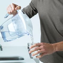 Warum Wasser filtern meist überflüssig ist Mann schenkt gefiltertes Leitungswasser in ein Glas ein