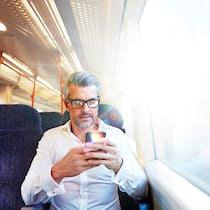 Apps, mit denen Sie alle Verkehrsmittel kombinieren Mann im Zug mit Smartphone