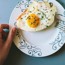 Warum Eiweisse so wichtig sind für eine gesunde Ernährung Eine Frau sitzt am Tisch, vor ihr liegt ein Spiegelei auf dem Teller.