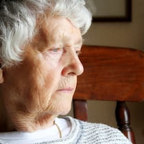Welche Anzeichen alarmieren sollten Eine Seniorin sitzt am Fenster und schaut mit schwermütigem Blick nach draussen.