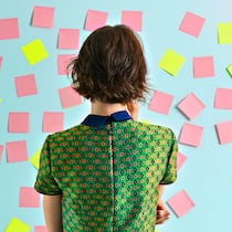 Zeit für einen neuen Job Eine Frau steht mit dem Rücken zur Kamera und blickt auf eine hellblaue Wand, die mit lauter rosa- und gelbfarbigen Post-its beklebt ist.
